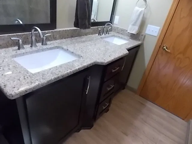 Finished bathroom with a dark double vanity and granite countertops, built by Powerbuilt Construction