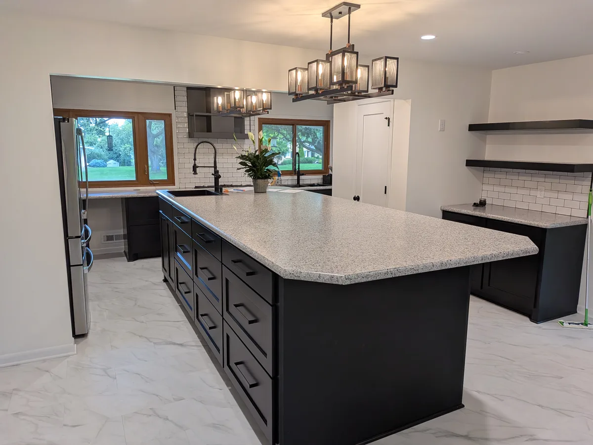 Finished kitchen with black cabinets, a large quartz island, and marble-look tile floor, remodeled by Powerbuilt Construction