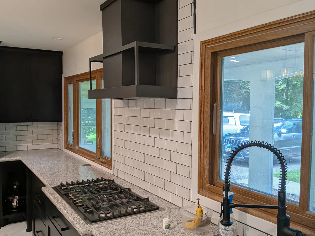 The same kitchen finished with black cabinets, granite counters, a custom black range hood, and a subway-tile backsplash, remodeled by Powerbuilt Construction