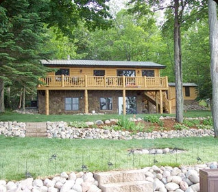 Lakeside cabin with a full-width deck and stone base, built by Powerbuilt Construction